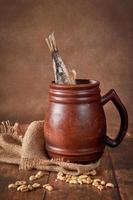 caneca marrom de barro de cerveja com cerveja e peixe seco em uma mesa de madeira em um fundo escuro. foto