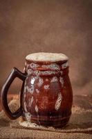 caneca de argila marrom de cerveja com kvass em uma mesa de madeira em um fundo escuro. uma bebida tradicional feita de pão, fermento foto