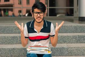 cara jovem estudante zangado com livros de joelhos foto