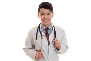 médico jovem bonito posando de uniforme e sorrindo isolado no fundo branco no estúdio foto