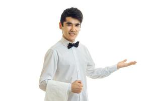 encantador garçom alegre com camisa de cabelo preto dá uma mãozinha para o lado e sorrindo foto