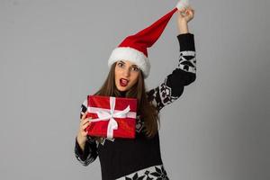 mulher de suéter quente e chapéu de Papai Noel com presente vermelho foto