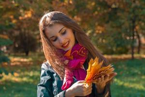 linda garota sorrindo mantém as folhas caídas de cabeça no parque foto