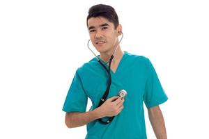 médico jovem bonito posando com estetoscópio de uniforme isolado no fundo branco no estúdio foto