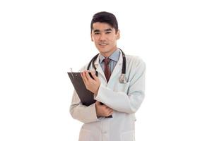 jovem médico de uniforme com estatoscópio faz anotações e sorrindo isolado no fundo branco foto