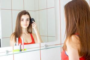 jovem sorridente se olha no espelho e penteia o pente de cabelo foto
