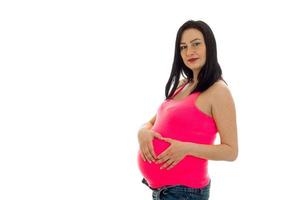 mulher morena grávida atraente com barriga grande posando de camisa rosa isolada no fundo branco foto