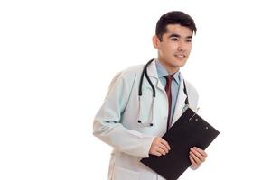 jovem médico bonito morena de uniforme com estetoscópio no pescoço posando e olhando para longe isolado no fundo branco foto