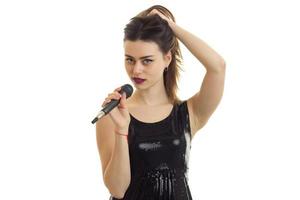 incrível jovem morena mantém o cabelo da mão e canta em um microfone foto