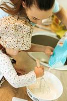 menina bonitinha caseira com sua linda mãe faz panquecas na cozinha branca. foto