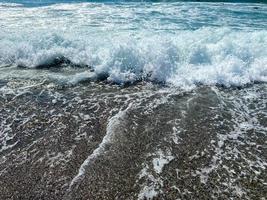 ondas de água no mar e areia com pequenas pedras multicoloridas naturais à beira-mar, pequenas pedras na praia. fundo, textura foto