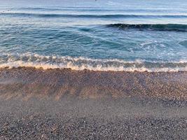 ondas de água no mar e areia com pequenas pedras multicoloridas naturais à beira-mar, pequenas pedras na praia. fundo, textura foto