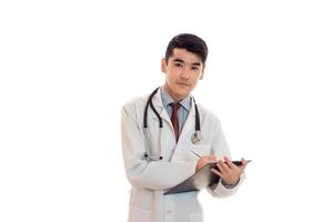 jovem médico masculino com estetoscópio de uniforme e fazer anotações isoladas no fundo branco foto