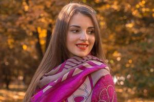 retrato de uma jovem atraente em um lenço rosa nos ombros que olha para o lado e sorri foto