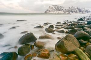 ondas fluindo sobre a praia de utakleiv, ilhas lofoten, noruega no inverno. foto