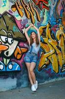 garota de macacão jeans posando contra a parede com graffiti foto