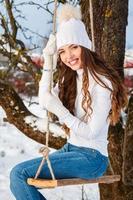 garota feliz no balanço da corda no dia ensolarado de inverno foto