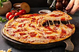 pizza de pepperoni com uma fatia retirada com puxador de queijo foto