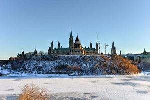 colina do parlamento e a casa do parlamento canadense em ottawa, canadá, do outro lado do rio ottawa congelado durante o inverno. foto