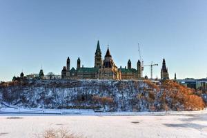 colina do parlamento e a casa do parlamento canadense em ottawa, canadá, do outro lado do rio ottawa congelado durante o inverno. foto