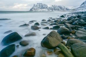 ondas fluindo sobre a praia de utakleiv, ilhas lofoten, noruega no inverno. foto