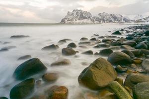 ondas fluindo sobre a praia de utakleiv, ilhas lofoten, noruega no inverno. foto