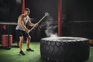 homem está batendo no pneu com uma marreta durante seu treino de cross training foto