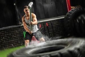 homem está batendo no pneu com uma marreta durante seu treino de cross training foto