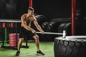 homem está batendo no pneu com uma marreta durante seu treino de cross training foto