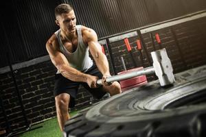 homem está batendo no pneu com uma marreta durante seu treino de cross training foto