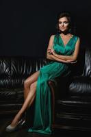 mulher vestindo lindo vestido de seda verde está posando no sofá de couro foto