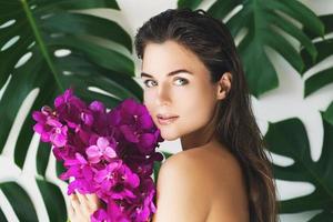 mulher jovem e bonita com pele lisa perfeita está segurando flores de orquídea foto