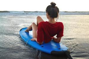 mulher sentada na prancha de surf na praia após sua sessão de surf foto