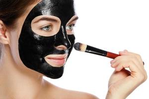 linda mulher está aplicando máscara preta purificadora no rosto foto