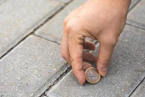 mão feminina pegando uma moeda de euro do chão foto