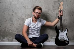 cara barbudo elegante com guitarra contra a parede de concreto foto
