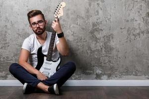 cara barbudo elegante com guitarra contra a parede de concreto foto