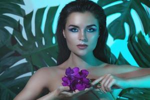 mulher jovem e bonita com pele lisa perfeita está segurando flores de orquídea foto