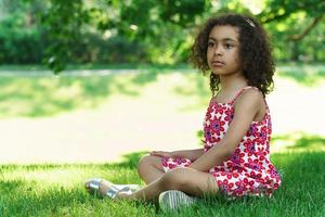 menina africana sentada em uma grama em um parque da cidade foto
