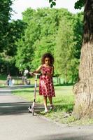 menina negra com uma patinete em um parque da cidade foto