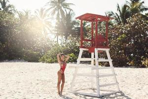 mulher sexy em maiô vermelho ao lado da torre de salva-vidas na praia foto