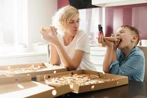 mãe e seu filho fofo comendo pizza deliciosa em casa foto