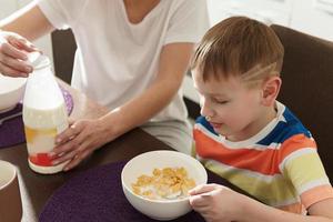 linda mãe e seu filho fofo comendo flocos de milho saudáveis no café da manhã foto