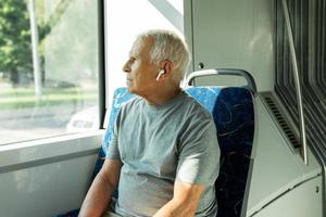 homem idoso está usando fones de ouvido sem fio durante passeio em transporte público foto