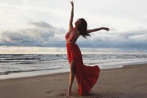 mulher deslumbrante usando lindo vestido vermelho na praia foto