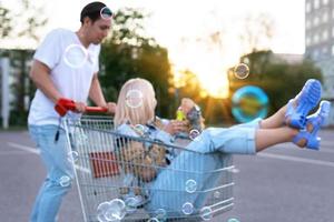 casal se diverte com um carrinho de compras e soprando bolhas no estacionamento de um supermercado foto