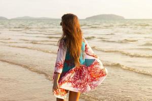 jovem linda mulher vestindo lindo vestido está caminhando à beira-mar foto