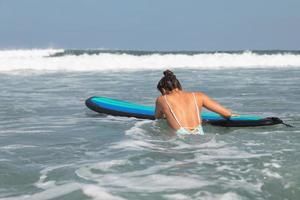 surfista mulher está tentando entrar em linha através de ondas durante seu treino de surf foto