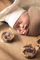 bebê recém-nascido com chapéu de chef está deitado na bandeja do forno com muffins foto