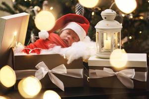 lindo bebê recém-nascido usando chapéu de papai noel está dormindo na caixa de presente de natal foto